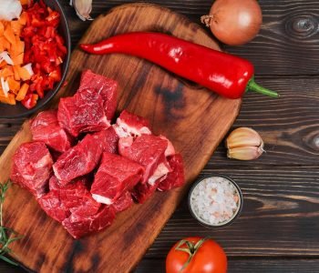 Layout of ingredients for cooking goulash or stew: raw beef meat, vegetables, spices, on a rustic wooden background. Top view, banner for website.